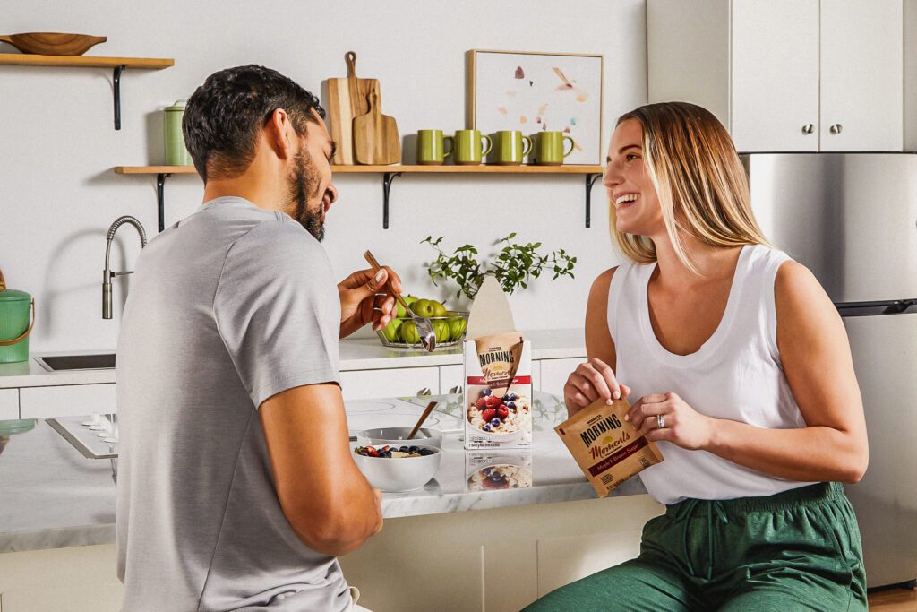 Ein Paar genießt sein Frühstück an einer Kücheninsel mit einem Instant-Haferflockenbeutel in der Hand