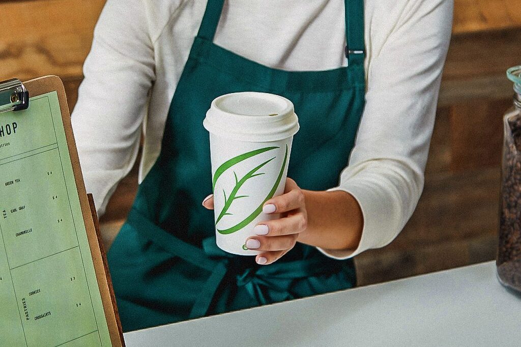 Ein Barista reicht jemandem Kaffee im Ecotainer-Heißgetränkebecher von Graphic Packaging